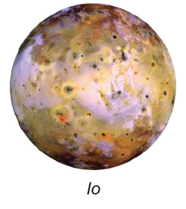 The image depicts Io, one of Jupiter's moons. It is a spherical celestial body characterized by a colorful and varied surface. The surface exhibits a mix of yellow, orange, brown, and white hues with scattered dark spots. The texture appears mottled with irregular patterns and features, including bright and dark patches. Some areas exhibit crater-like formations and surface variations, suggesting geological activity.