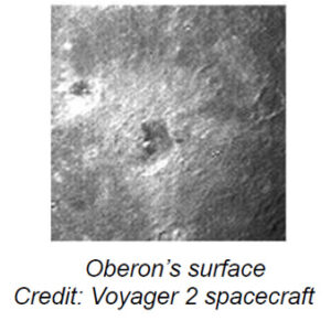 The image depicts a grayscale surface view of Oberon, one of Uranus's moons. The terrain appears rugged and cratered, with a prominent large crater slightly off-center to the left. The surface is marked by numerous smaller craters and depressions scattered throughout. The texture suggests a rough, uneven landscape, typical of celestial bodies with histories of impacts.