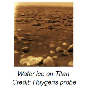 The image depicts a landscape on Saturn's moon Titan. It shows a barren and rocky terrain under an overcast sky. The foreground contains smooth, rounded stones of various sizes, scattered across a flat surface. The stones appear to have a reflective quality. Further into the distance, the terrain becomes progressively indistinct, with a hazy atmosphere obscuring the horizon. The entire scene is bathed in a sepia tone, giving it a monochromatic brownish-orange appearance.