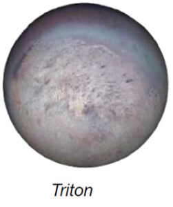 The image depicts Neptune's moon Triton, showing a spherical celestial body with a textured surface. The predominant color is a muted, dusty beige with variations of light and dark patches across the surface, suggesting craters or geological formations. The moon is slightly illuminated, with subtle shadowing that accentuates its topography. A faint blue hue encircles the upper portion, contributing to a slightly ethereal appearance.