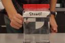 Woman's hand holding a white and black circle illustration behind water in a jar labeled "shower"